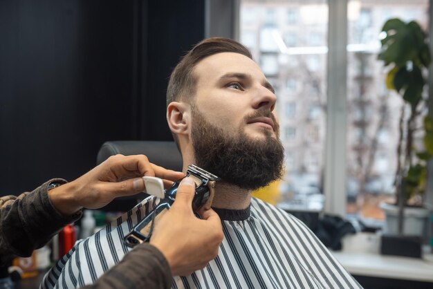 Hombre visitando estilista en peluquería. Barber trabaja con un cortapelos. Cliente inconformista cortándose el pelo.