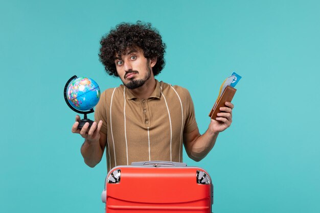 Hombre de vista frontal en vacaciones sosteniendo globo y boleto en azul claro