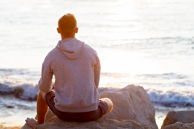 Hombre de vista posterior relajante en la playa con espacio de copia