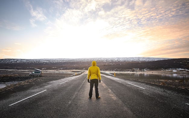 Hombre vistiendo una chaqueta amarilla mientras está de pie en medio de una carretera vacía mirando en la distancia