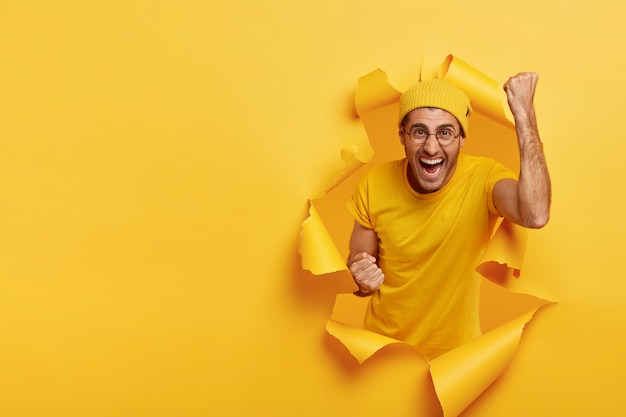 Hombre vítores alegre posando a través de papel rasgado