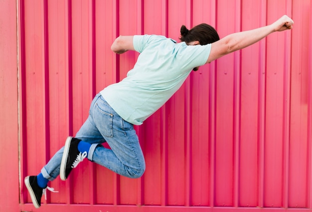 Hombre volando con los brazos levantados contra la pared de color rosa corrugado