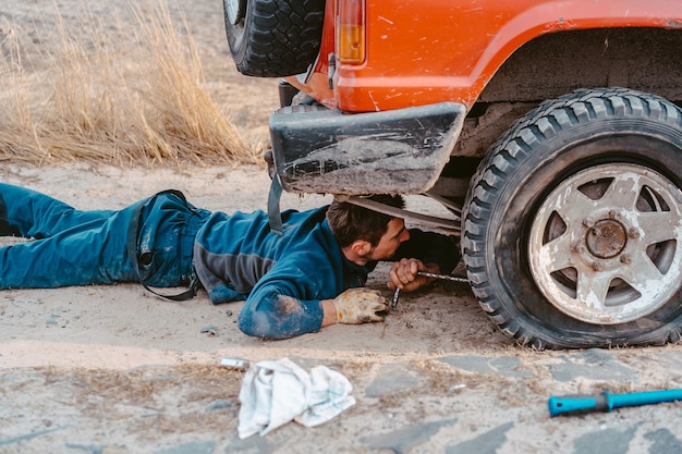 El hombre yace debajo de un automóvil 4x4 en un camino de tierra