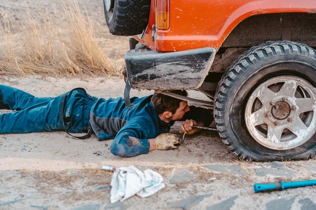 El hombre yace debajo de un automóvil 4x4 en un camino de tierra