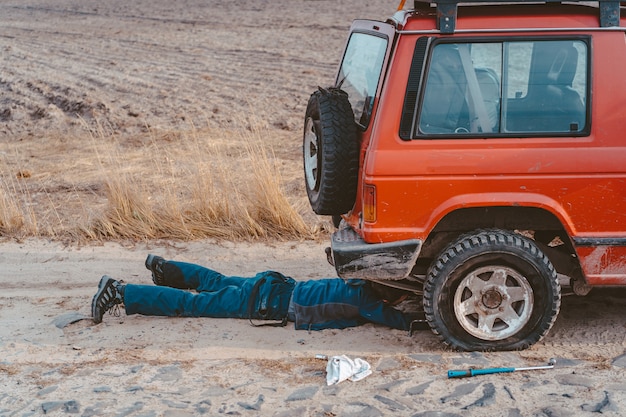 El hombre yace debajo de un automóvil 4x4 en un camino de tierra