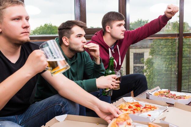 Hombres aficionados viendo fútbol en la televisión y bebiendo cerveza. Tres hombres bebiendo cerveza y divirtiéndose juntos en el bar.