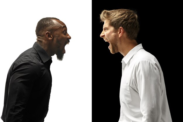 Los hombres afro y caucásicos gritando. Pareja mixta. Imagen dinámica de modelos masculinos en estudio blanco y negro. Concepto de emociones faciales humanas.