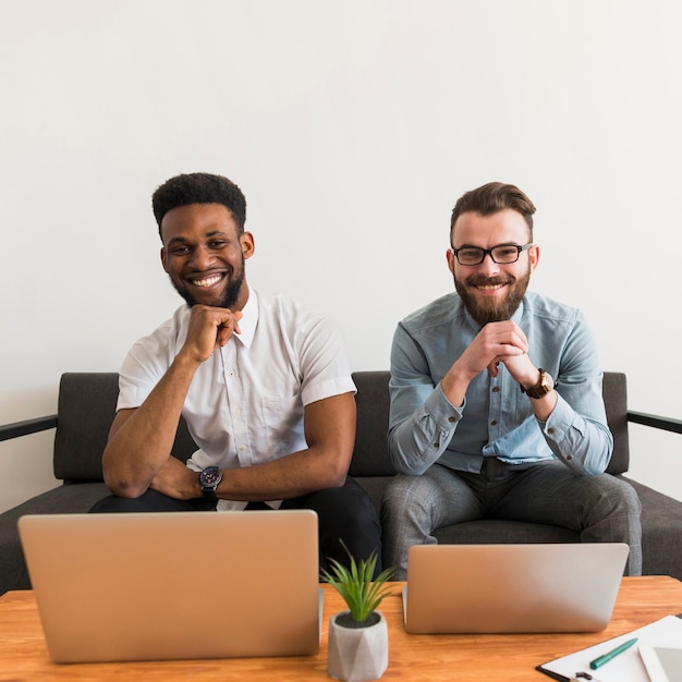 Hombres alegres cerca de computadoras portátiles