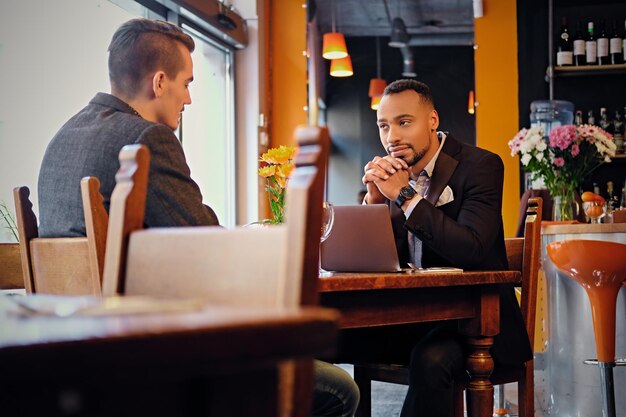 Hombres americanos caucásicos y negros que tienen una reunión de negocios en un restaurante.
