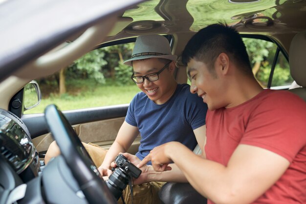 Hombres asiáticos felices sentados en el coche y mirando a la cámara juntos
