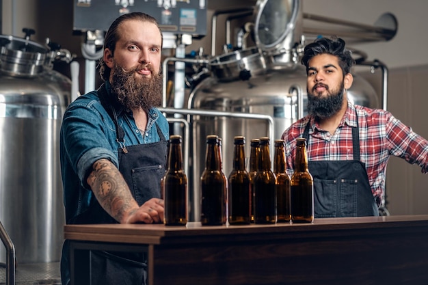 Hombres caucásicos e indios barbudos tatuados presentando cerveza artesanal en la microcervecería.