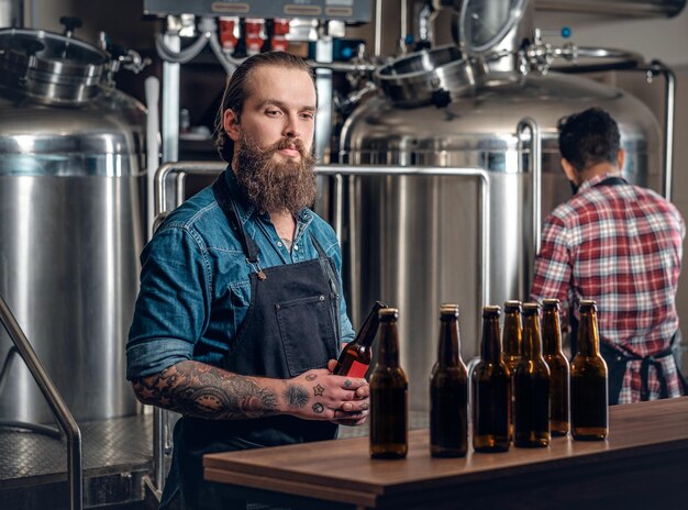 Hombres caucásicos e indios barbudos tatuados presentando cerveza artesanal en la microcervecería.