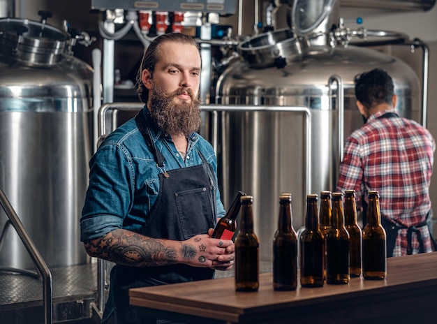 Hombres caucásicos e indios barbudos tatuados presentando cerveza artesanal en la microcervecería.