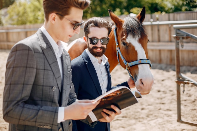 Hombres elegantes de pie junto al caballo en un rancho