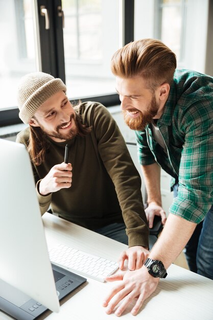 Hombres felices colegas en la oficina usando la computadora. Mirando a un lado