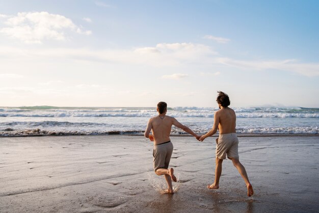 Hombres gay de tiro completo tomados de la mano en la playa