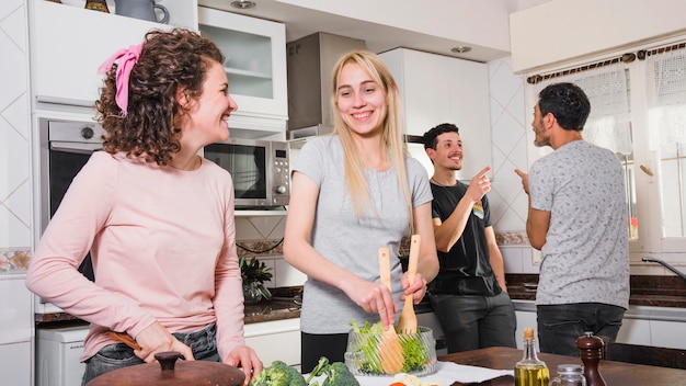 Hombres hablando entre ellos y mujeres preparando ensaladas en la mesa de la cocina.