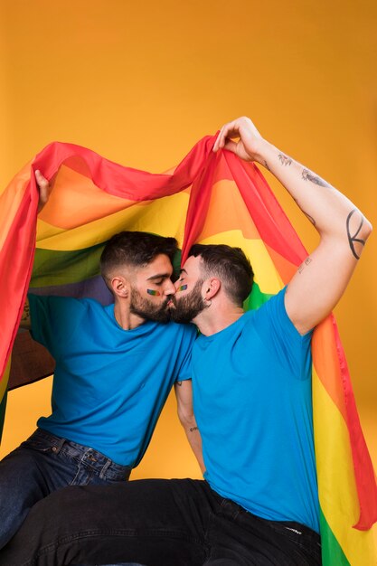 Hombres jóvenes besándose bajo bandera LGBT