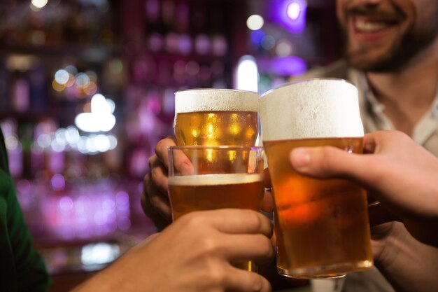 Hombres jóvenes brindando con cerveza mientras están sentados juntos en un pub