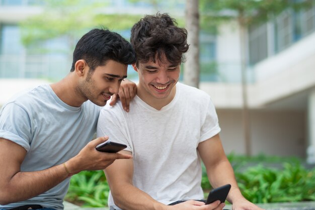 Hombres jovenes emocionados alegres que discuten aplicaciones del smartphone