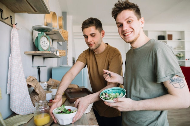 Hombres jovenes felices que comen jugo de la ensalada y de fruta en cocina