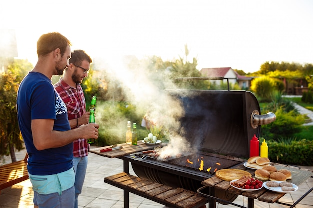 Hombres jovenes que asan la barbacoa en parrilla en campo de la cabaña.