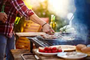 Foto gratuita hombres jovenes que asan la barbacoa en parrilla en campo de la cabaña.