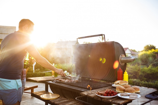 Hombres jovenes que asan la barbacoa en parrilla en campo de la cabaña.