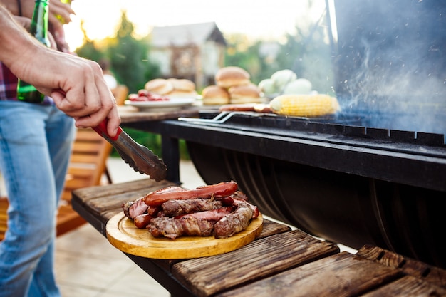 Hombres jovenes que asan la barbacoa en parrilla en campo de la cabaña.