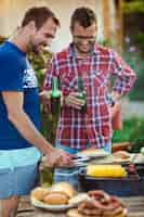 Foto gratuita hombres jovenes que asan la barbacoa en parrilla en campo de la cabaña.