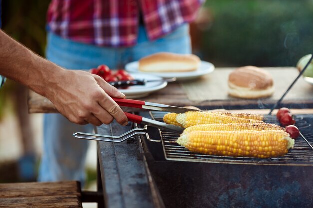 Hombres jovenes que asan la barbacoa en parrilla en campo de la cabaña.