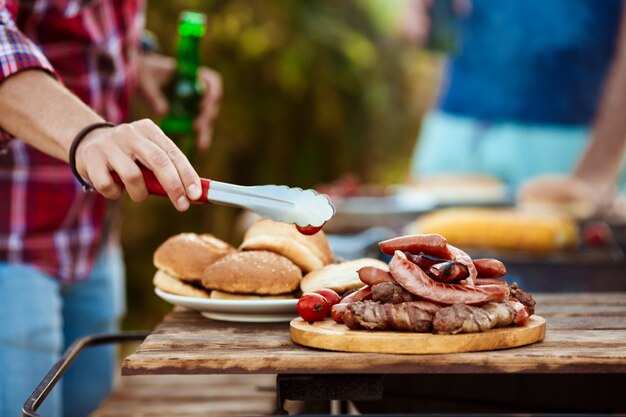 Hombres jovenes que asan la barbacoa en parrilla en campo de la cabaña.