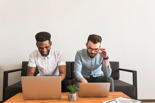 Hombres jóvenes que navegan computadoras portátiles en el sofá