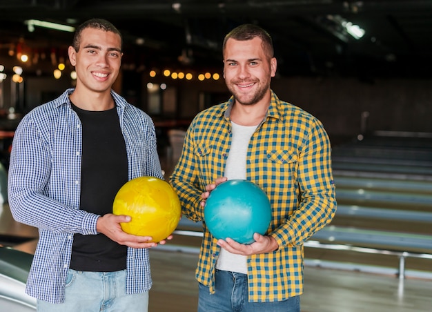 Hombres jovenes que sostienen bolas de bolos coloridas