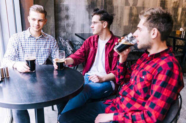 Hombres jóvenes sentados juntos bebiendo la cerveza con su amigo