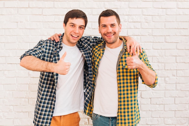 Hombres jovenes sonrientes con sus brazos alrededor de su hombro que muestra el pulgar encima de la muestra