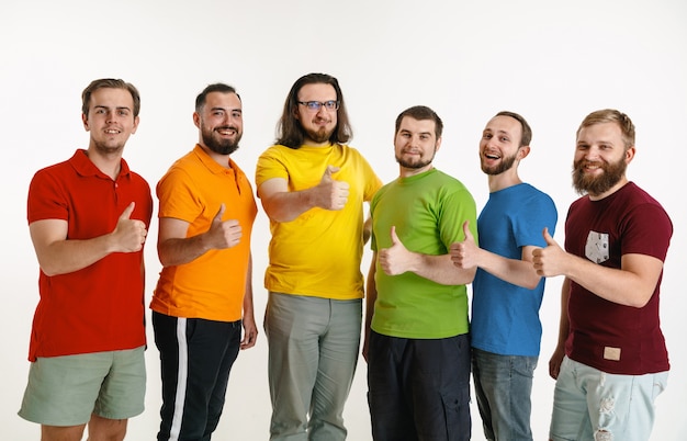 Los hombres jóvenes vestían los colores de la bandera LGBT aislados en la pared blanca. Modelos masculinos caucásicos en camisetas de color rojo, naranja, amarillo, verde, azul y morado. Orgullo LGBT, derechos humanos y concepto de elección.