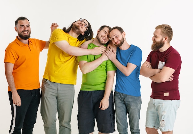 Los hombres jóvenes vestían los colores de la bandera LGBT aislados en la pared blanca. Modelos masculinos caucásicos en camisetas de color rojo, naranja, amarillo, verde, azul y morado. Orgullo LGBT, derechos humanos y concepto de elección.