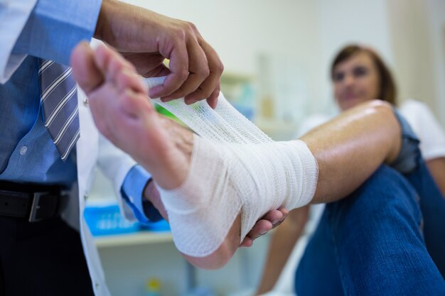 Hombres médico de vendaje del pie del paciente femenino