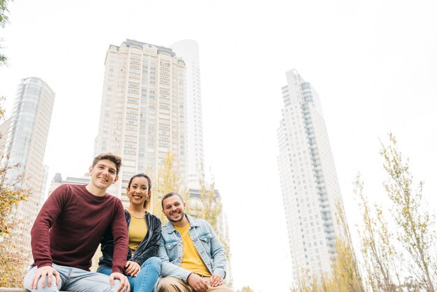 Hombres y mujer sonrientes multirraciales que se sientan junto en parque del otoño de la ciudad