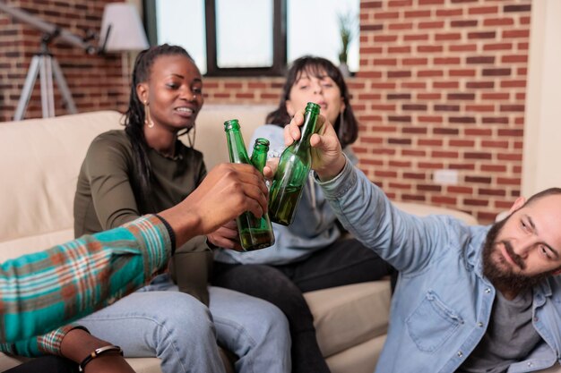 Hombres y mujeres haciendo gestos de alegría y tintineando botellas de cerveza, brindando por una reunión de amistad en una reunión divertida. Gente alegre haciendo tostadas con bebidas alcohólicas, actividad de ocio.