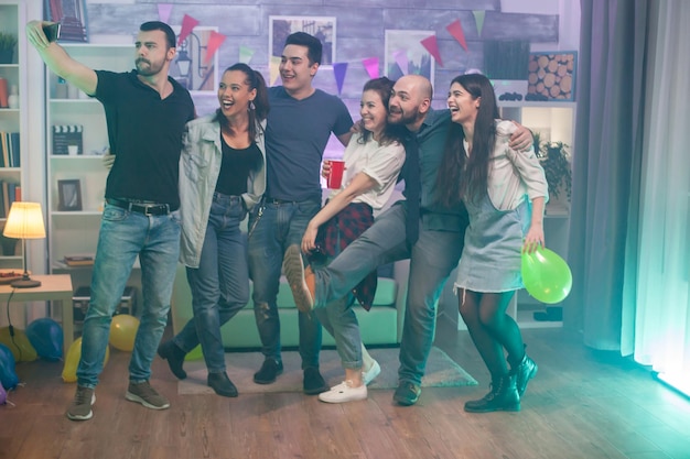 Hombres y mujeres jóvenes felices y alegres tomándose un selfie mientras celebran su amistad.