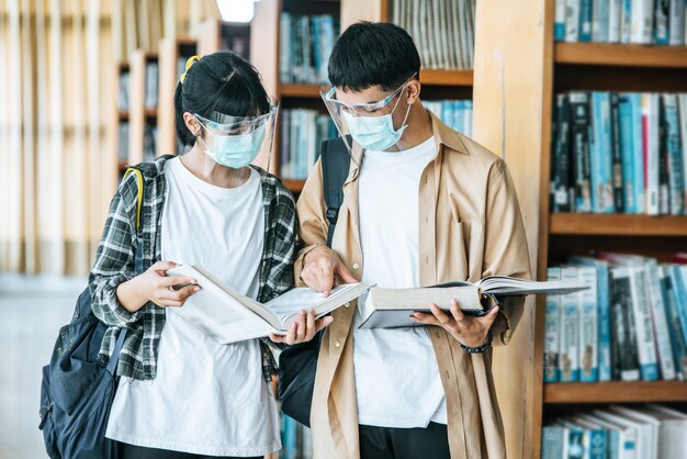 Hombres y mujeres con máscaras se paran y leen en la biblioteca.