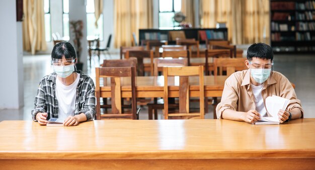 Hombres y mujeres con máscaras se sientan y leen en la biblioteca.