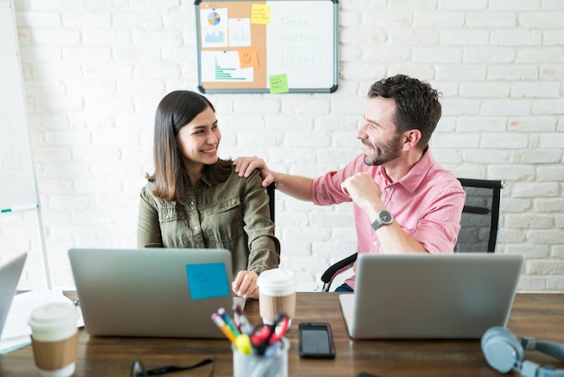 Hombres y mujeres de negocios sonrientes que se comunican mientras usan una computadora portátil en el escritorio de la oficina