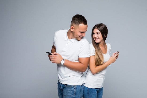 Hombres y mujeres pareja joven de pie con teléfonos móviles en sus manos aisladas sobre fondo gris
