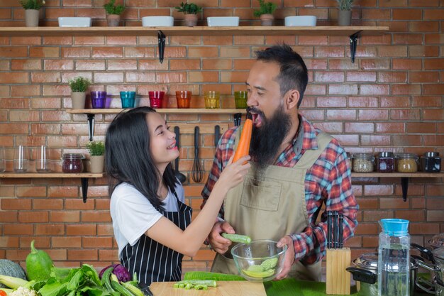 Hombres y mujeres que se burlan mientras cocinan en la cocina con una pared de ladrillo rojo.