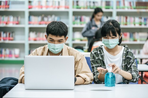 Hombres y mujeres usan máscaras y usan una computadora portátil para buscar libros en la biblioteca.