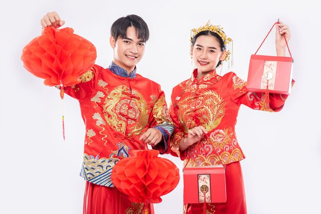 Hombres y mujeres vistiendo cheongsam de pie sosteniendo una bolsa roja y una linterna de panal