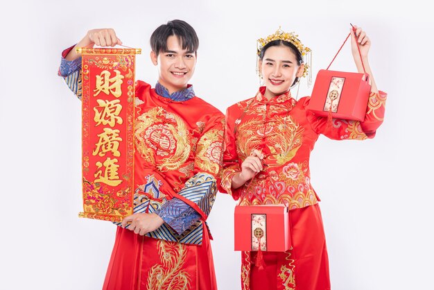 Hombres y mujeres vistiendo cheongsam de pie, sosteniendo carteles de saludo y llevando bolsas rojas